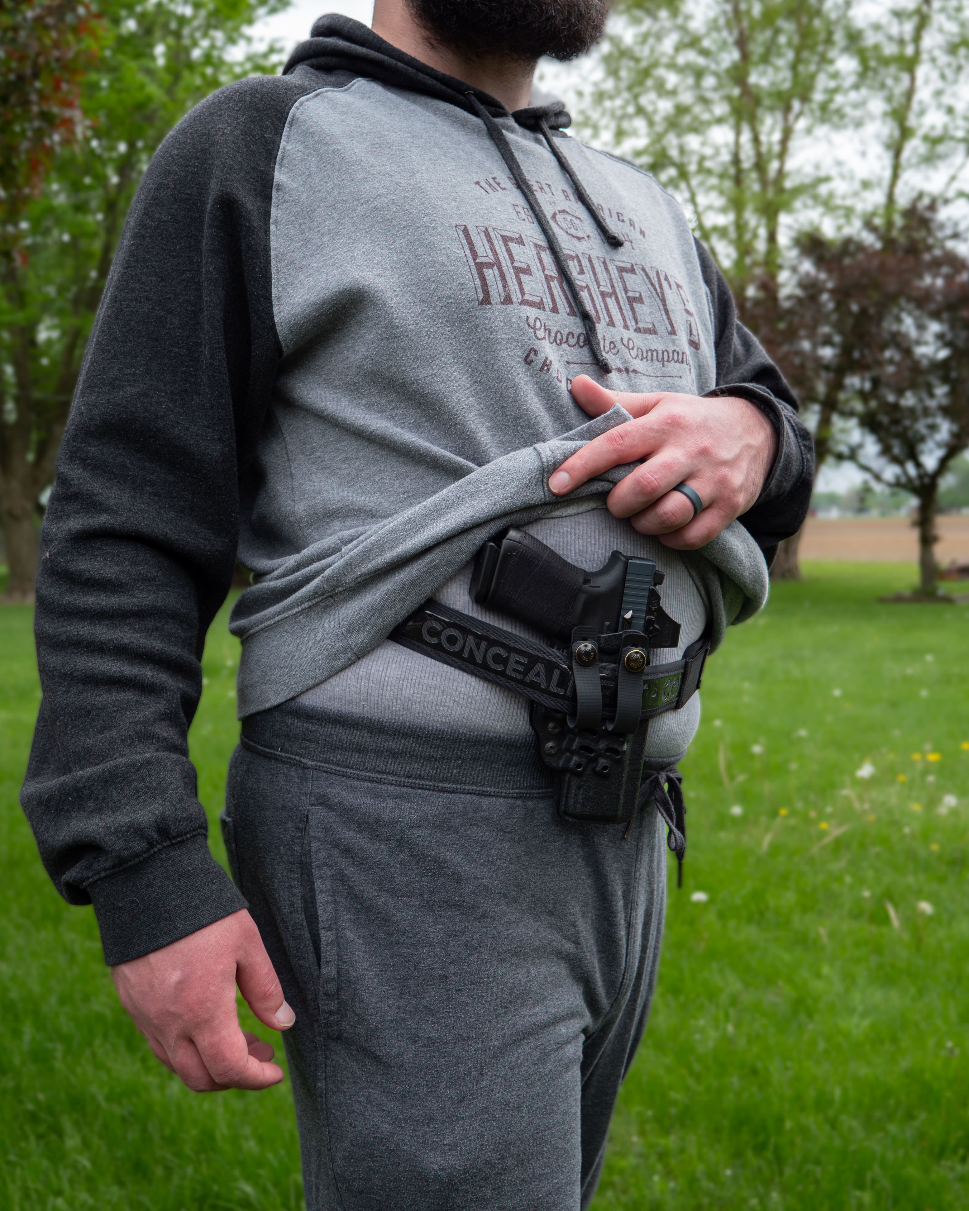 Man in a hoodie and joggers showing a holster carried on the BLACKOUT 2.0 belt outdoors